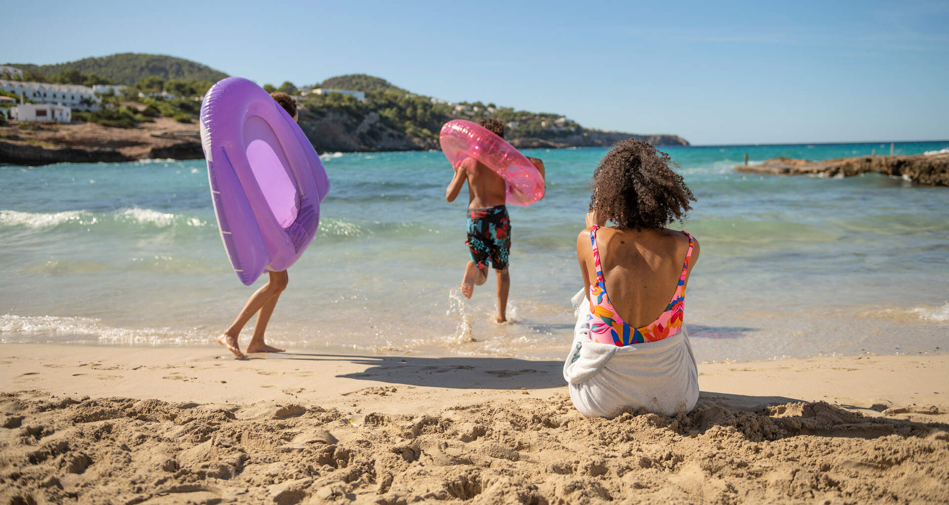 Mor med to børn leger i vandkanten mens de nyder en ferie de har booket med Sunwebs familierabat