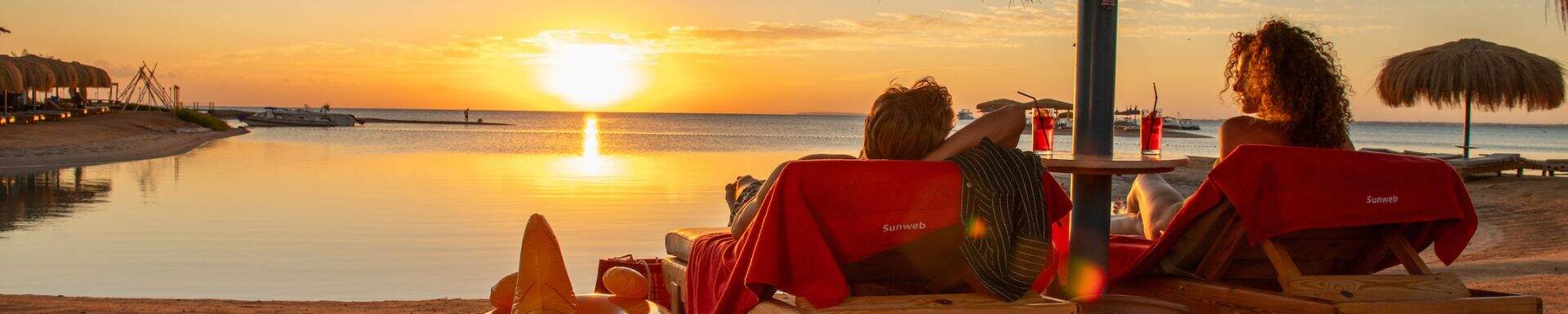 Par nyder solnedgangen med en drink ved hjælp af et messetilbud fra Sunweb